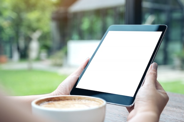 Image maquette d'une femme tenant un tablet pc noir avec un écran blanc blanc avec une tasse de café sur la table