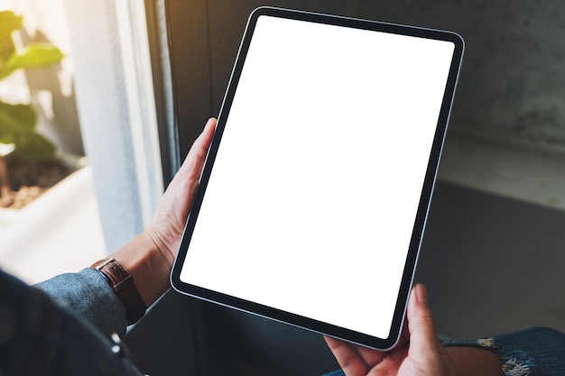 Image maquette d'une femme tenant un tablet pc noir avec un écran blanc vierge dans un café