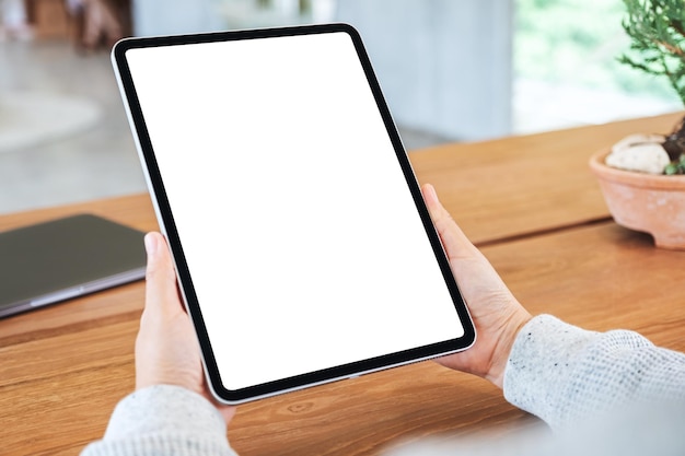 Image maquette d'une femme tenant un tablet pc noir avec un écran blanc vierge sur une table en bois