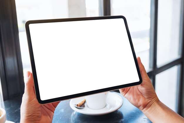 Image maquette d'une femme tenant un tablet pc noir avec un écran blanc vierge avec une tasse de café sur la table