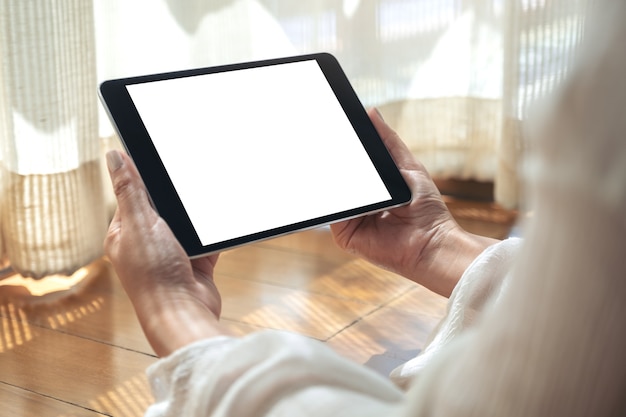 Image de maquette d'une femme tenant un tablet pc noir avec écran de bureau blanc vierge horizontalement tout en fixant le sol avec une sensation de détente