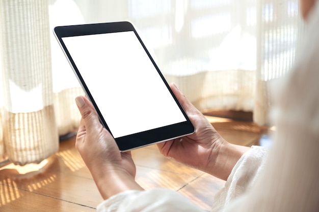 Image de maquette d'une femme tenant un tablet pc noir avec écran de bureau blanc vierge tout en fixant sur le sol avec une sensation de détente