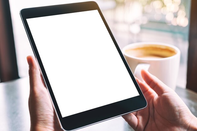 Image De Maquette D'une Femme Tenant Une Tablette Noire Avec Un écran Blanc Blanc Et Une Tasse De Café Sur La Table