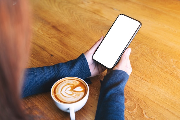 Image de maquette d'une femme tenant un téléphone portable blanc avec un écran blanc avec une tasse de café sur une table en bois