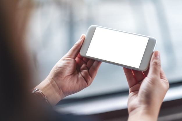 Image de maquette d'une femme tenant un téléphone portable blanc avec un écran de bureau vierge dans un café