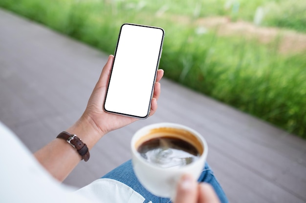 Image maquette d'une femme tenant un téléphone portable avec un écran de bureau blanc vierge tout en buvant du café à l'extérieur