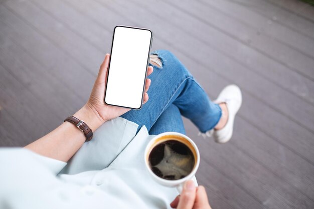 Image maquette d'une femme tenant un téléphone portable avec un écran de bureau blanc vierge tout en buvant du café à l'extérieur
