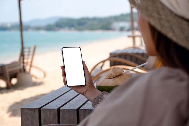 Image maquette d'une femme tenant un téléphone portable avec un écran de bureau vierge assis sur la plage