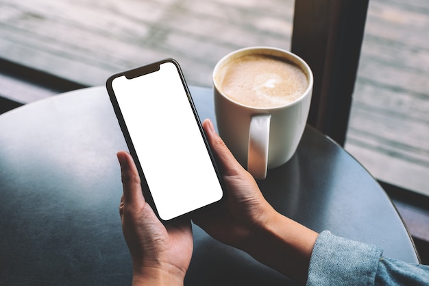 Image maquette d'une femme tenant un téléphone portable noir avec écran blanc avec une tasse de café sur la table