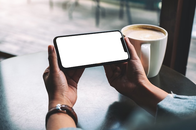 Image maquette d'une femme tenant un téléphone portable noir avec écran blanc avec une tasse de café sur la table