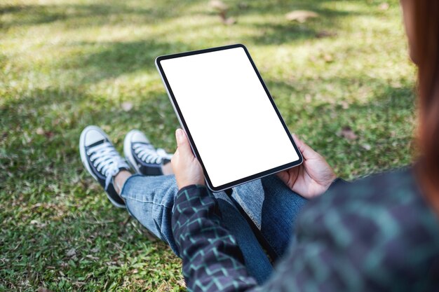 Image maquette d'une femme tenant et utilisant un tablet pc noir avec un écran de bureau blanc vierge alors qu'il était assis à l'extérieur