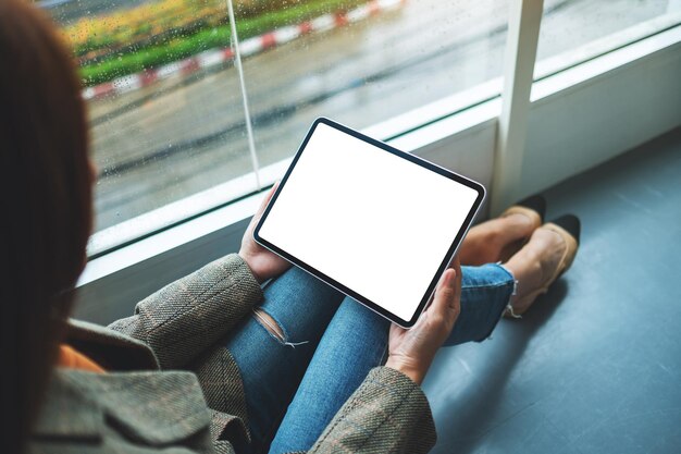 Image maquette d'une femme tenant et utilisant une tablette numérique avec un écran de bureau blanc vierge alors qu'elle était assise sur le sol