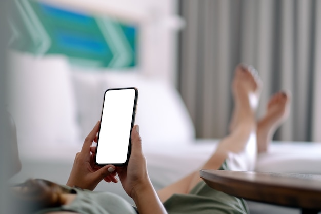 Image de maquette d'une femme tenant et utilisant un téléphone mobile avec écran blanc tout en vous relaxant et allongé sur le lit