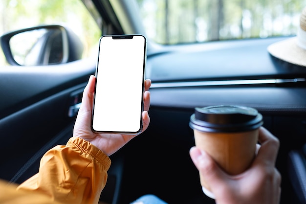Image maquette d'une femme tenant et utilisant un téléphone portable avec écran vide tout en buvant du café dans la voiture