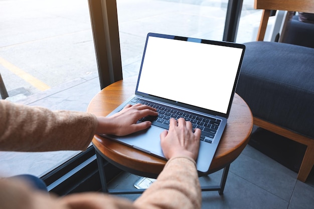 Image maquette d'une femme utilisant et tapant sur un ordinateur portable avec un écran de bureau blanc vierge sur une table en bois dans un café