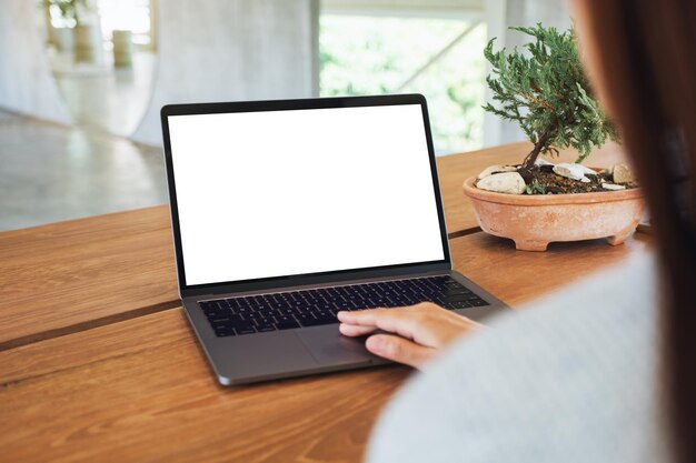 Image maquette d'une femme utilisant et touchant le pavé tactile d'un ordinateur portable avec un écran de bureau blanc vierge sur une table en bois