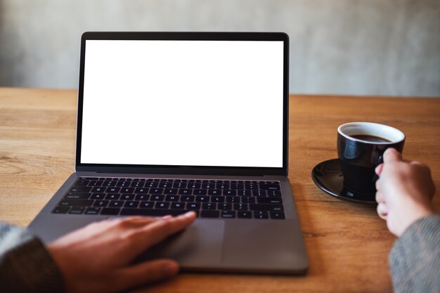 Image maquette d'une femme utilisant et touchant le pavé tactile d'un ordinateur portable avec un écran de bureau blanc vierge tout en buvant du café