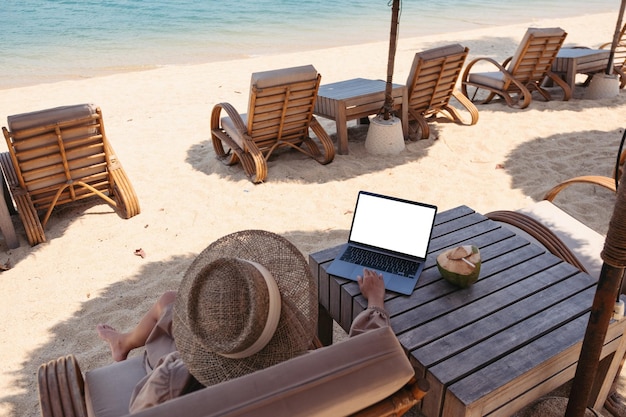 Image maquette d'une femme utilisant et touchant le pavé tactile d'un ordinateur portable avec un écran de bureau vierge tout en étant assise sur la plage