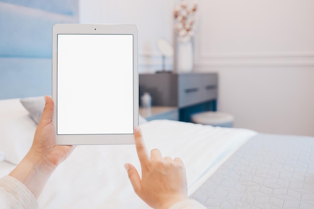 Image maquette de la main d'une femme tenant une tablette blanche avec un écran blanc vierge à la maison