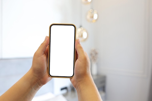 Image maquette de la main d'une femme tenant un téléphone avec un écran blanc vierge à la maison