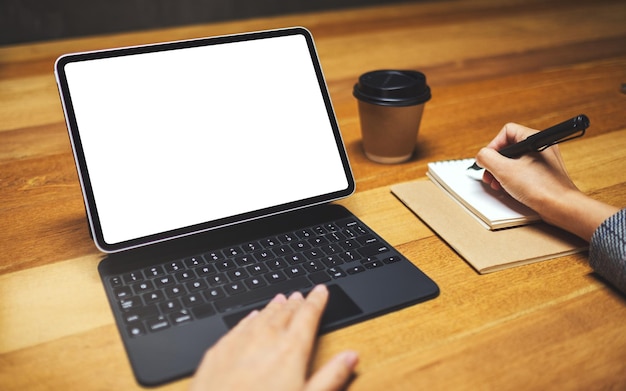 Image maquette d'une main utilisant et touchant le pavé tactile de la tablette avec un écran de bureau blanc vierge comme ordinateur tout en écrivant et en travaillant, une tasse à café sur une table en bois