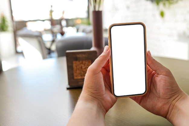 Image maquette des mains d'une femme tenant un téléphone portable blanc avec écran vide au café