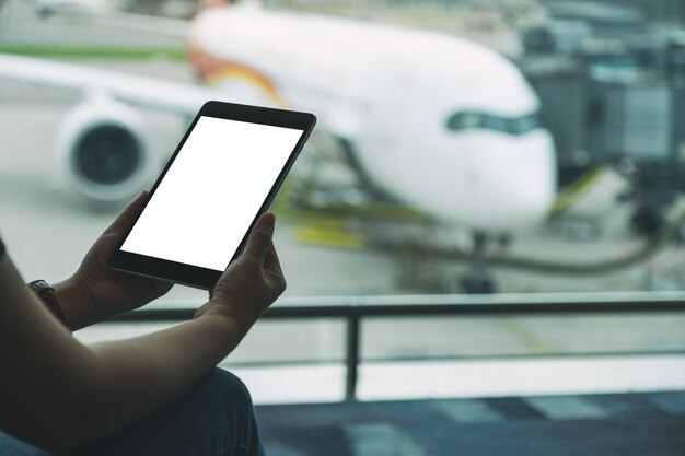 Image maquette des mains d'une femme tenant et utilisant une tablette noire avec un écran blanc vierge alors qu'elle était assise à l'aéroport