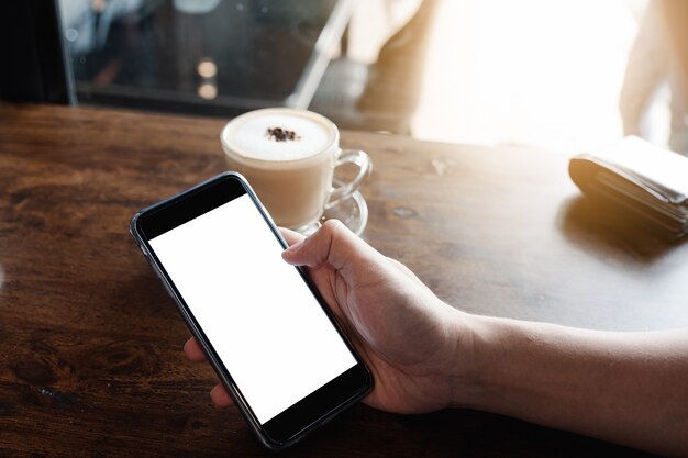 Image maquette de mains d&#39;homme tenant un téléphone portable blanc avec écran blanc dans un café moderne