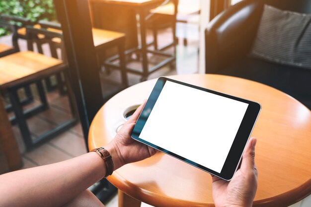 Image de maquette de mains tenant un tablet pc noir avec un écran blanc vierge avec une tasse de café sur une table en bois