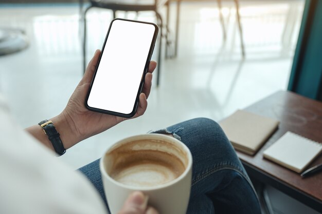 Image de maquette de mains tenant un téléphone mobile blanc avec écran blanc tout en buvant du café