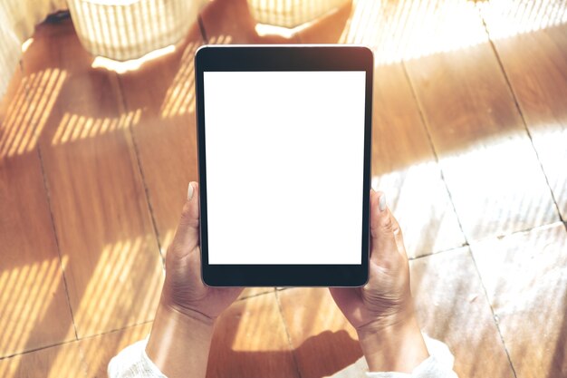 Image de maquette vue de dessus d'une femme tenant un tablet pc noir avec écran de bureau blanc vierge tout en fixant sur le plancher en bois