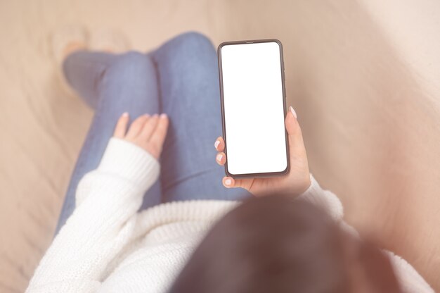 Image de maquette vue de dessus femme tenant un téléphone portable avec un écran de bureau vierge alors qu'elle était assise dans la chambre