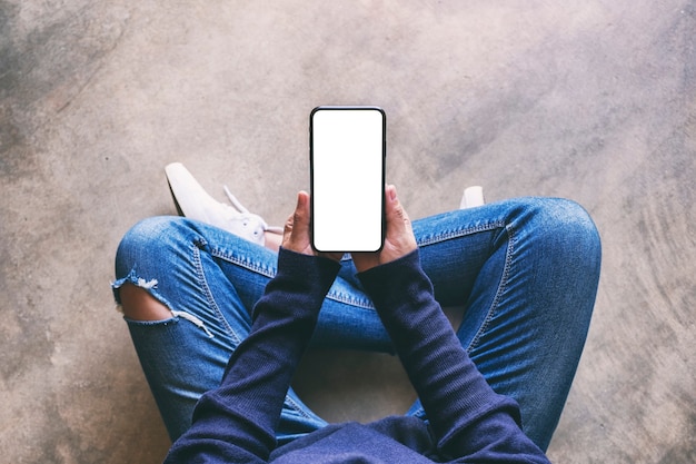 Image de maquette vue de dessus d'une femme tenant un téléphone portable noir avec un écran blanc vierge alors qu'elle était assise sur le sol