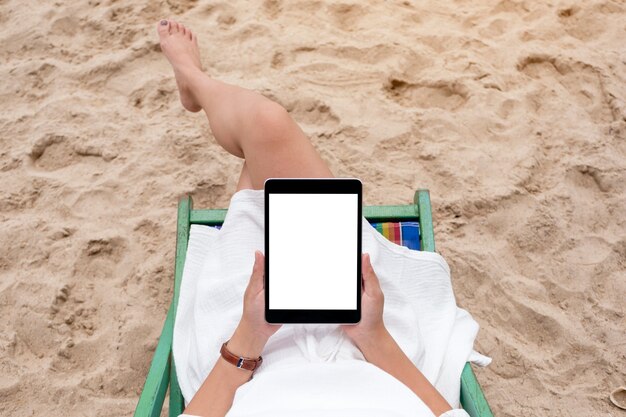 Image de maquette vue de dessus d'une femme tenant et utilisant une tablette noire avec un écran de bureau vide en position couchée sur une chaise de plage