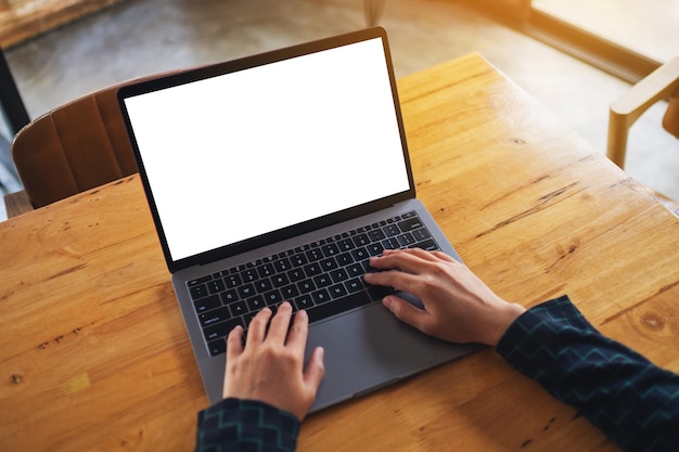 Image de maquette vue de dessus d'une femme utilisant et tapant sur un ordinateur portable avec un écran de bureau blanc vierge sur une table en bois