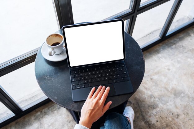 Image de maquette vue de dessus d'une main utilisant et touchant le pavé tactile de la tablette avec un écran de bureau blanc vierge comme ordinateur avec une tasse à café sur la table