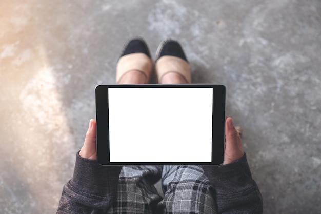 Image De Maquette Vue De Dessus Des Mains De Femme Tenant Et à L'aide De Tablet Pc Noir Avec écran De Bureau Blanc Vide Horizontalement Alors Qu'il était Assis Sur Le Sol