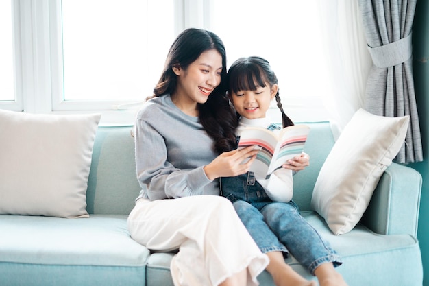 Image de la mère et de la fille assises sur le canapé en lisant un livre