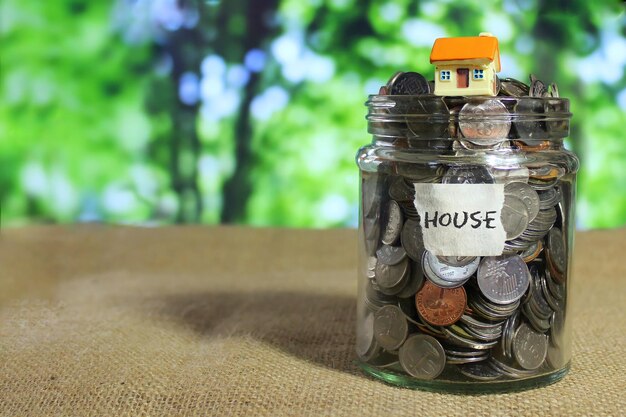 Image de mise au point sélective d'une mini maison sur des pièces de monnaie dans un bocal en verre