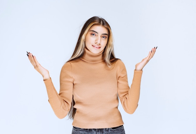 Image d'un modèle de jeune femme en pull marron debout et levant les mains.