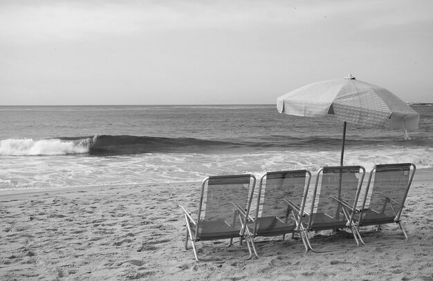 Image monochrome d'un groupe de chaises de plage vides avec parasol sur la plage de sable