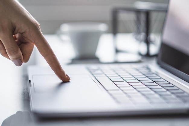 L'image montre les mains d'une femme tapant sur un clavier d'ordinateur portable élégant avec l'environnement du bureau apparaissant flou en arrière-plan