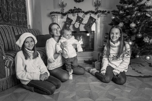 Image en noir et blanc d'une grande famille heureuse assise sur le sol à la cheminée à Noël