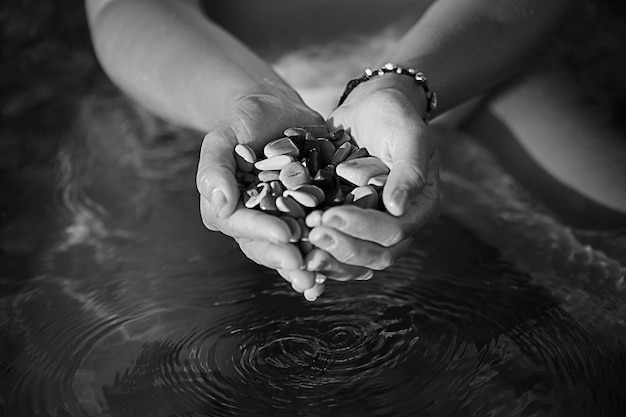 Image en noir et blanc des mains jointes avec les pierres de la mer sur le fond arroser les gouttes