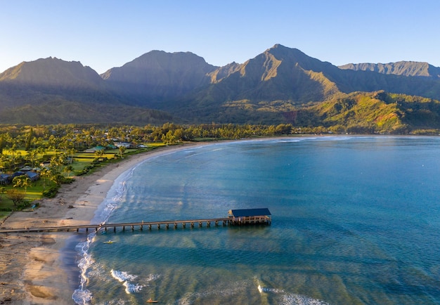 Image panoramique aérienne au lever du soleil au large de la côte sur la baie d'Hanalei et la jetée sur l'île hawaïenne de Kauai