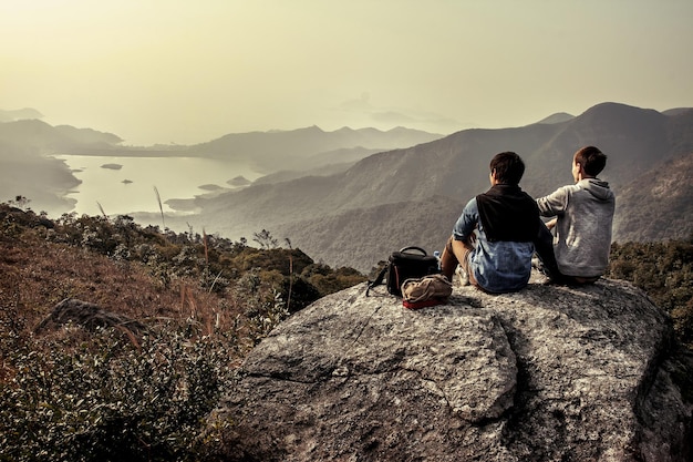 Image de personnes assises sur un gros rocher tout en regardant au loin le paysage