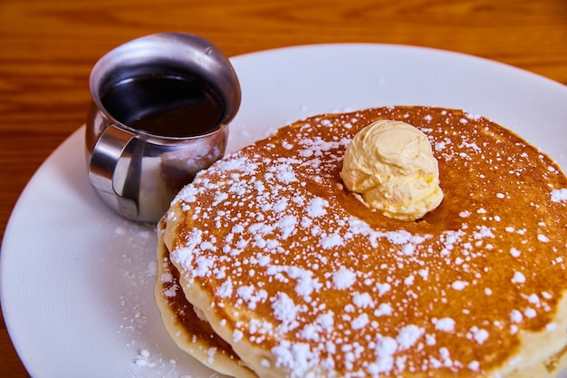 Image d'une pile classique de crêpes saupoudrées de sucre en poudre et garnies d'une cuillerée de beurre