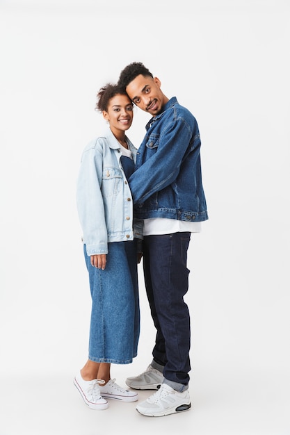 Image pleine longueur du couple africain souriant en chemises en jean posant ensemble sur un mur gris