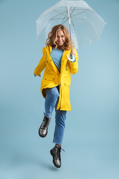 Image pleine longueur de jeune femme de 20 ans portant un imperméable jaune debout sous un parapluie transparent