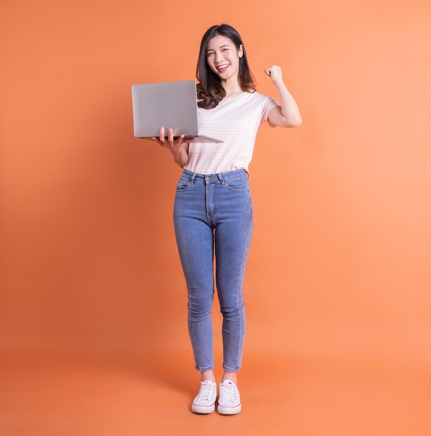 Image pleine longueur d'une jeune fille asiatique utilisant un ordinateur portable sur fond orange